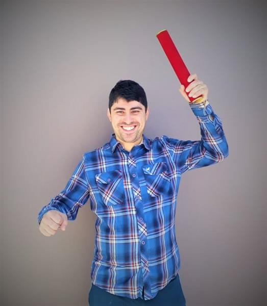 #pracegover: um jovem rapaz, comemorando sua graduação de expressão feliz erguendo o canudo de formatura
